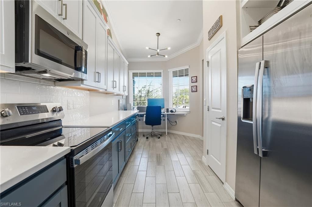 Dual tone kitchen with stainless steel appliances, ornamental molding, wood finish floors, tasteful backsplash, and hanging lights