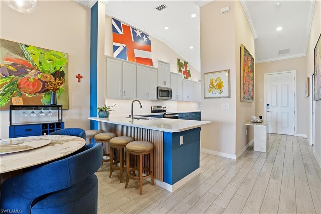 Kitchen with a kitchen breakfast bar, a peninsula, wood finish floors, stainless steel appliances, and crown molding