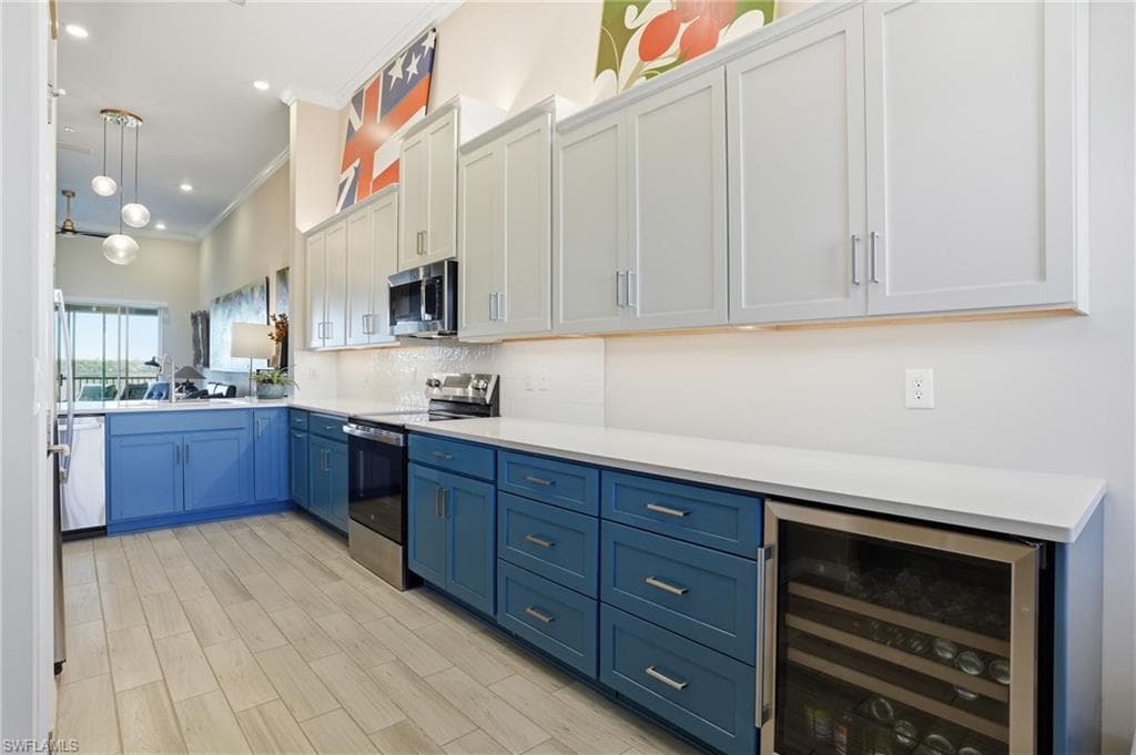 Two tone kitchen featuring stainless steel appliances, beverage cooler, two tone color scheme, crown molding, and hanging light fixtures