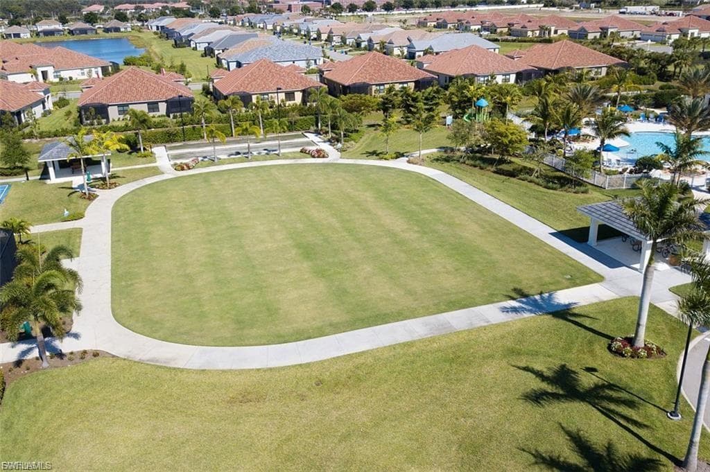 Expansive green lawn surrounded by a paved pathway, featuring mature palm trees and landscaped grounds