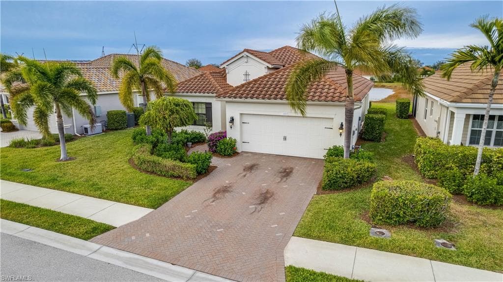 Mediterranean / spanish-style house with a garage, decorative driveway, a front yard, stucco siding, and a tiled roof