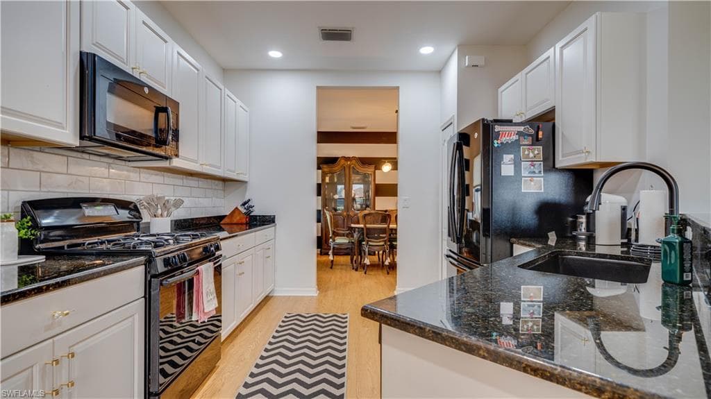 Kitchen with black appliances, white cabinets, dark stone countertops, light wood-style flooring, and recessed lighting