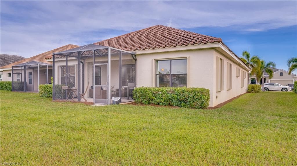 Rear view of house with stucco siding, a lanai, a yard, a tile roof, and a sunroom