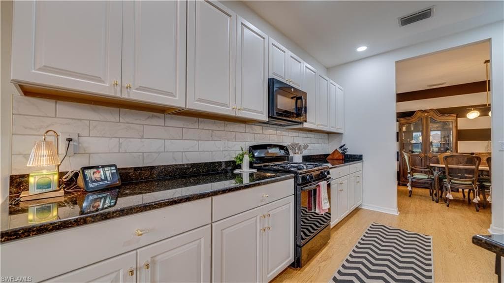 Kitchen with black appliances, white cabinets, dark stone counters, light wood finished floors, and recessed lighting