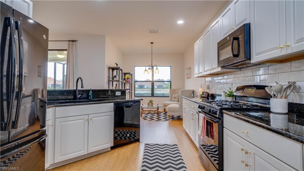 Kitchen with black appliances, white cabinetry, and dark stone countertops