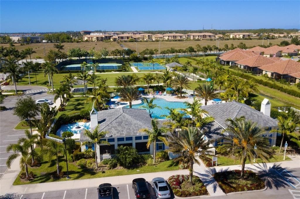 Community amenities featuring a central swimming pool, club-style building, multiple tennis courts, and lush tropical landscaping