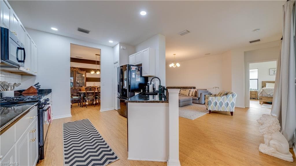Kitchen featuring dark stone countertops, black appliances, hanging lights, white cabinetry, and light wood-type flooring