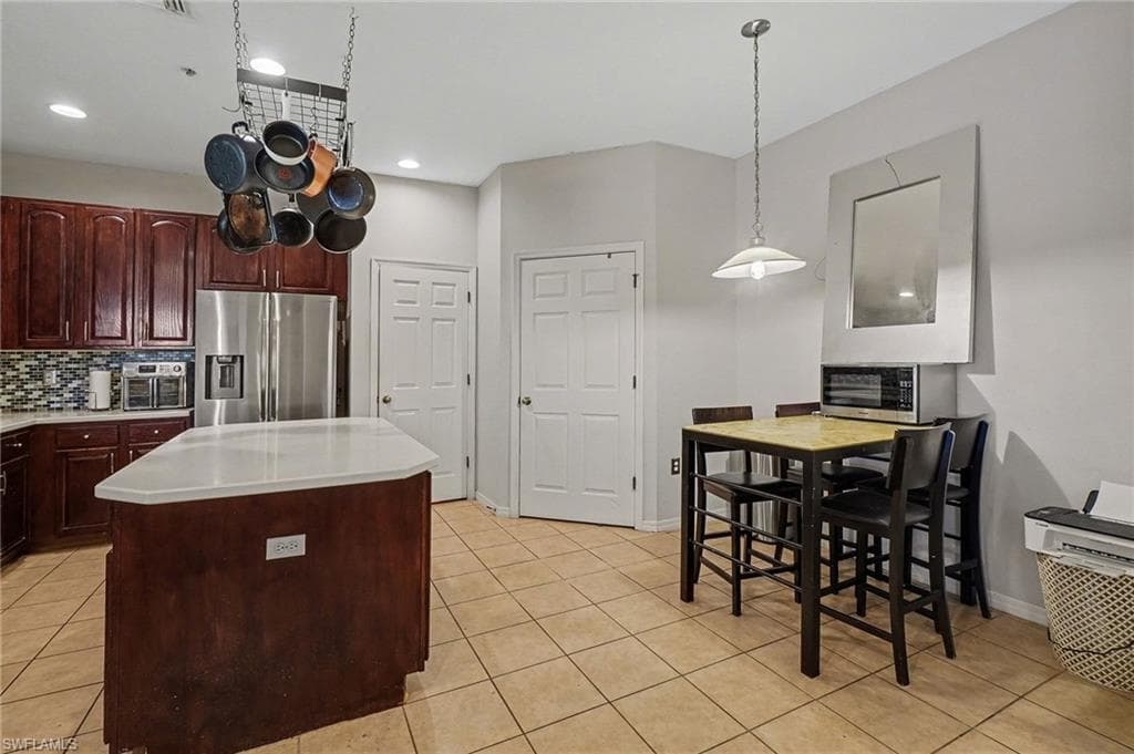 Kitchen with a kitchen island, stainless steel appliances, backsplash, light tile patterned floors, and hanging light fixtures