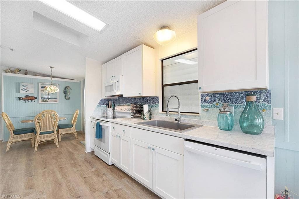 Kitchen with white appliances, white cabinets, light wood-style flooring, a textured ceiling, and pendant lighting