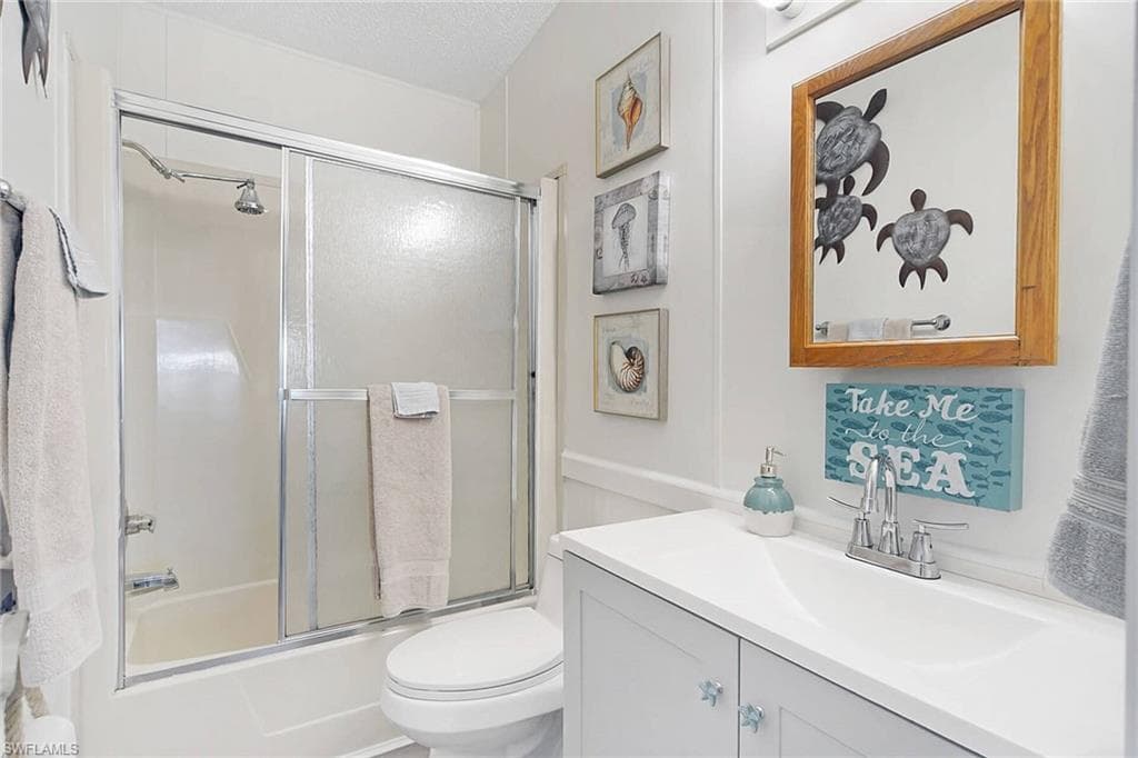 Full bath with vanity, combined bath / shower with glass door, a textured ceiling, and a wainscoted wall