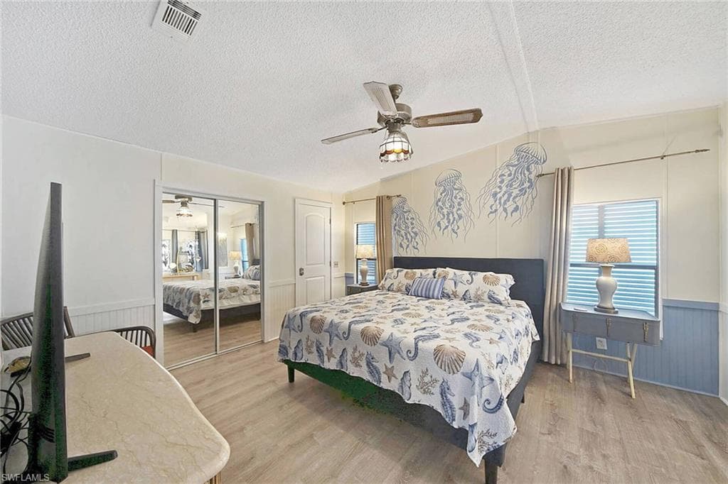 Bedroom with wainscoting, light wood-style floors, a ceiling fan, a closet, and wooden walls