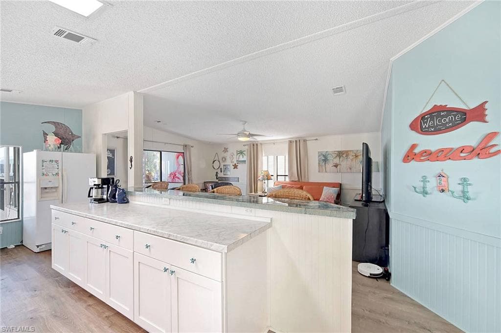 Kitchen with white refrigerator with ice dispenser, light countertops, open floor plan, light wood-style flooring, and a kitchen island