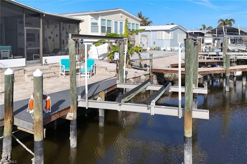 Dock area with boat lift, a water view, a sunroom, and a patio area
