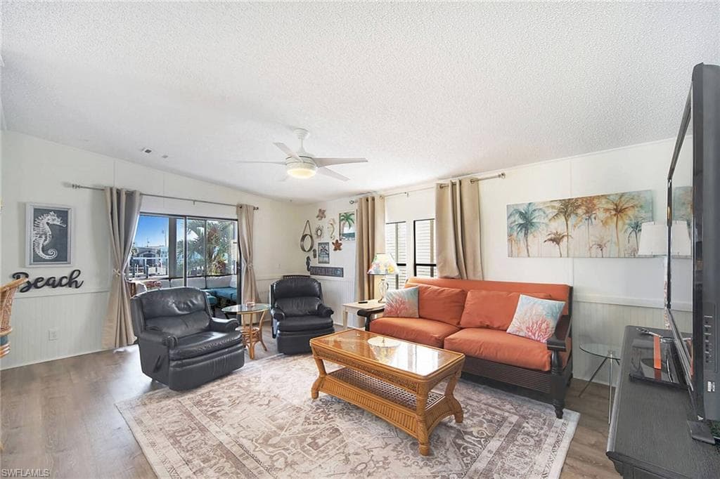 Living area featuring a wainscoted wall, wood finished floors, a textured ceiling, ceiling fan, and wood walls
