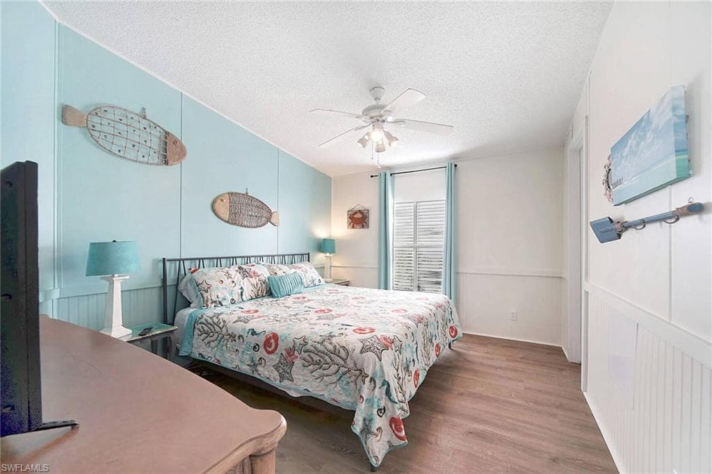 Bedroom featuring a textured ceiling, wood finished floors, ceiling fan, a decorative wall, and wainscoting