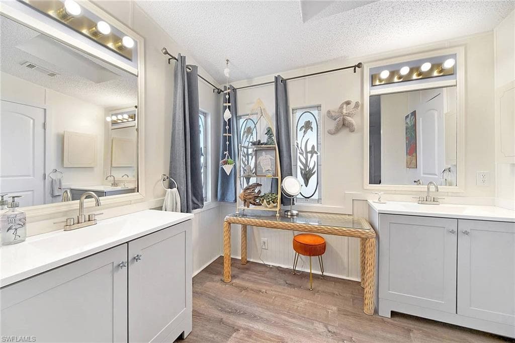 Full bath featuring a textured ceiling, two vanities, and light wood-style floors