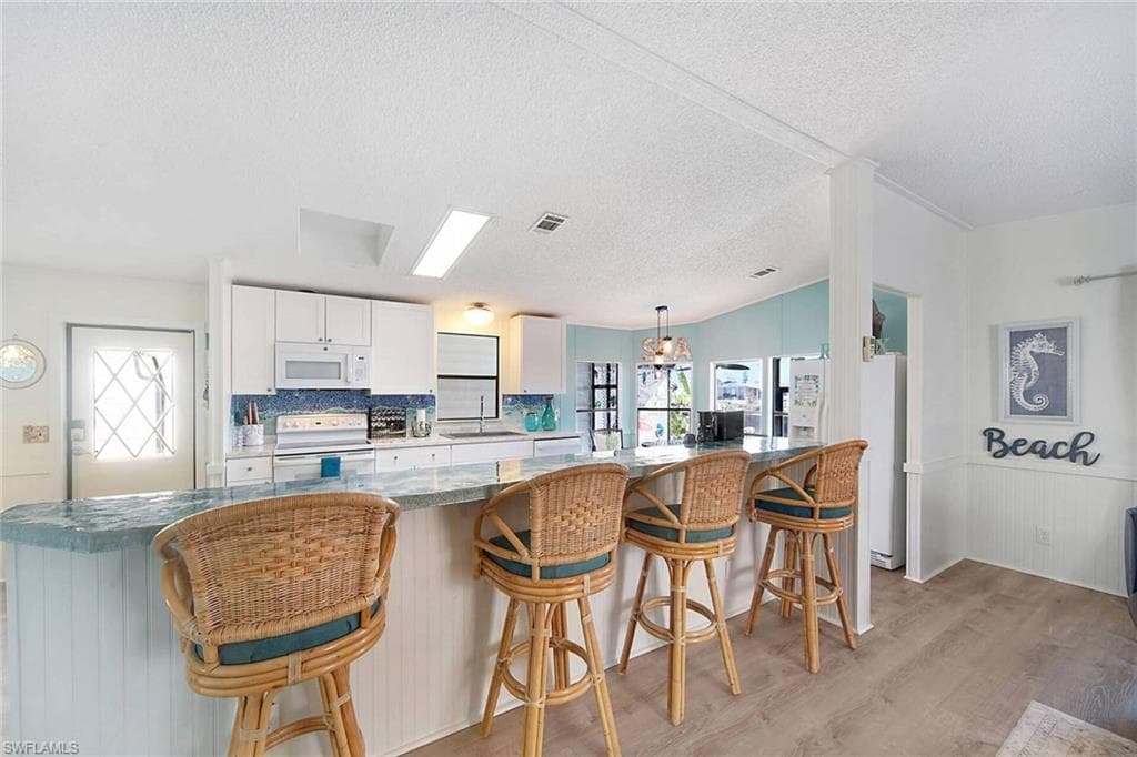 Kitchen with white appliances, a breakfast bar, white cabinetry, and light wood-style floors