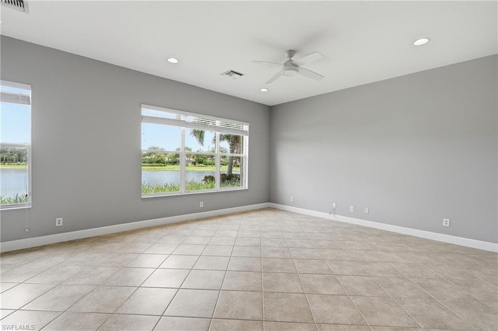 Expansive room featuring a window wall overlooking a body of water, neutral tile flooring, recessed lighting, a ceiling fan, and white baseboards