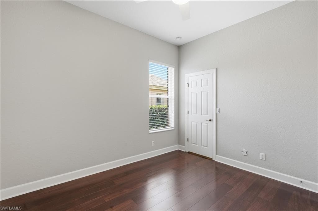 Room featuring dark wood-finish flooring, light grey painted walls, white baseboards, and a white paneled door