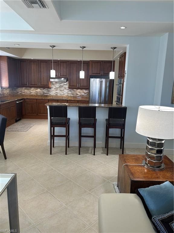 Kitchen featuring a kitchen breakfast bar, light tile patterned floors, fridge, hanging light fixtures, and backsplash