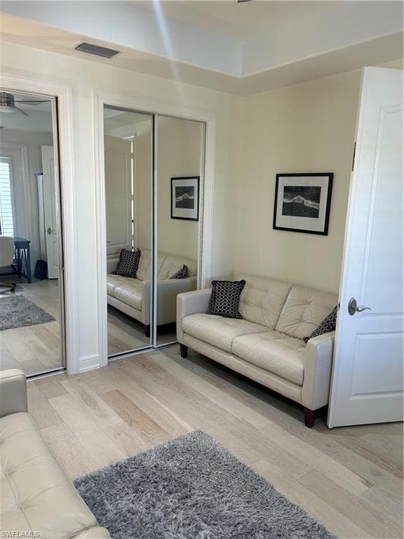 Den with ceiling fan, light wood-style floors and mirrored closets