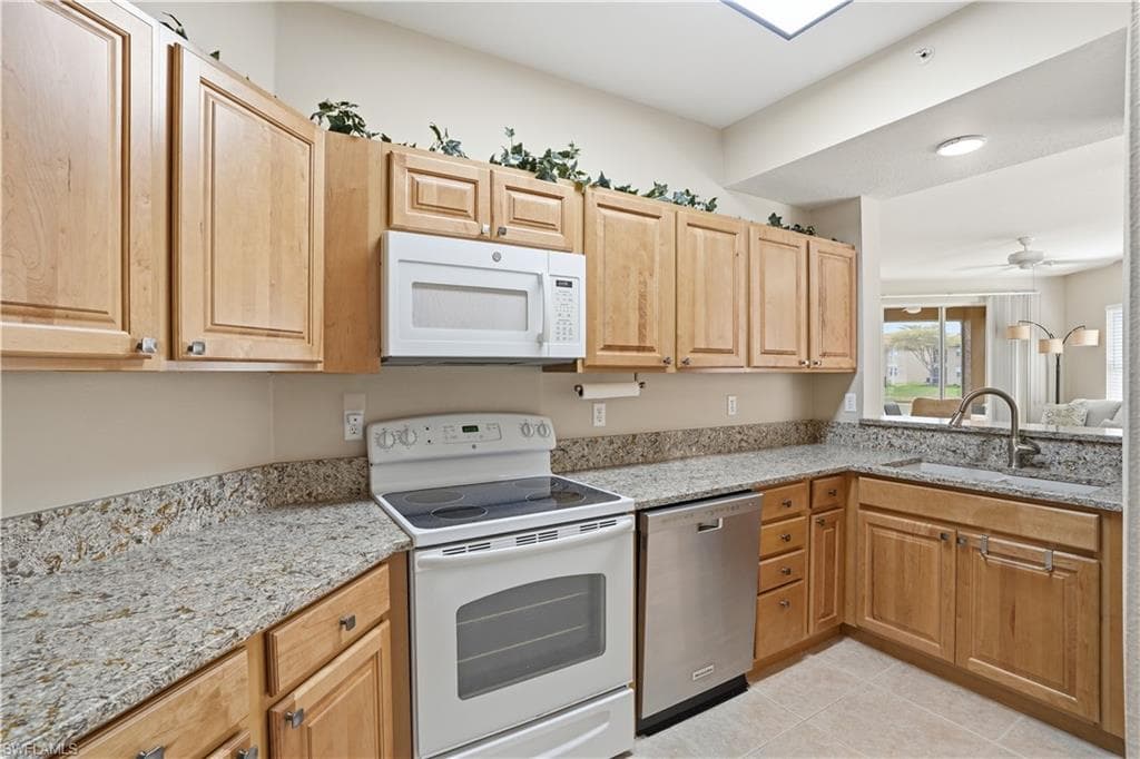 Kitchen with white appliances, light stone countertops, light wood finish cabinetry, ceiling fan, and light tile patterned flooring