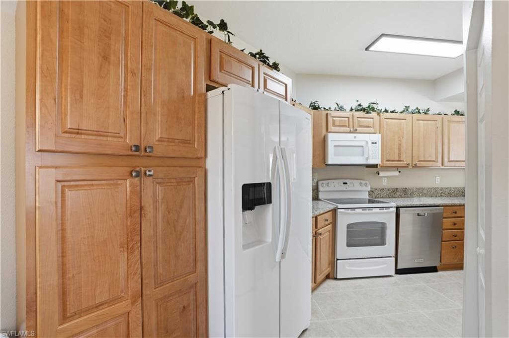 Kitchen with white appliances, light wood finish cabinets, light tile patterned flooring, and light stone countertops