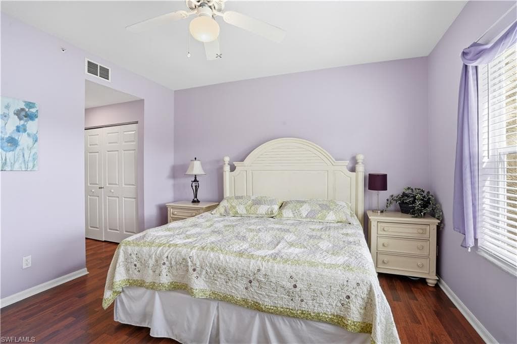 Bedroom with a closet, a ceiling fan, dark wood-style flooring, and multiple windows
