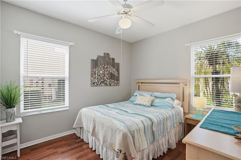 Bedroom with dark wood-style floors, ceiling fan, and multiple windows