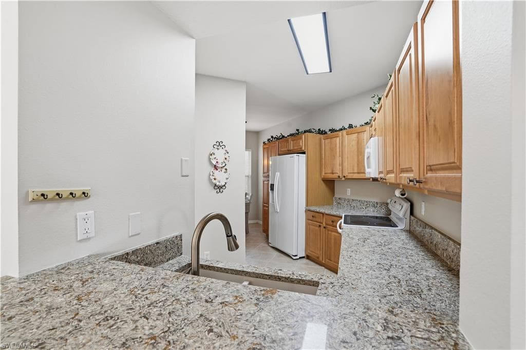 Kitchen with white appliances, light stone countertops, and light tile patterned flooring