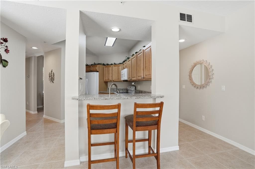 Kitchen featuring a breakfast bar area, light tile patterned flooring, white appliances, light stone counters, and recessed lighting