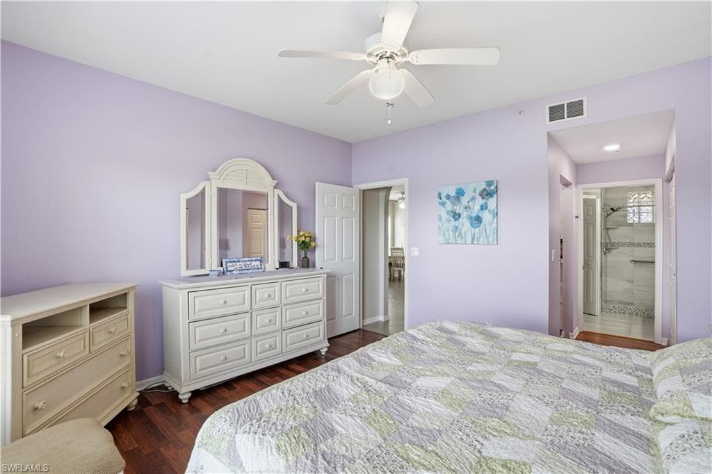 Bedroom with dark wood-style floors, ceiling fan, and connected bathroom
