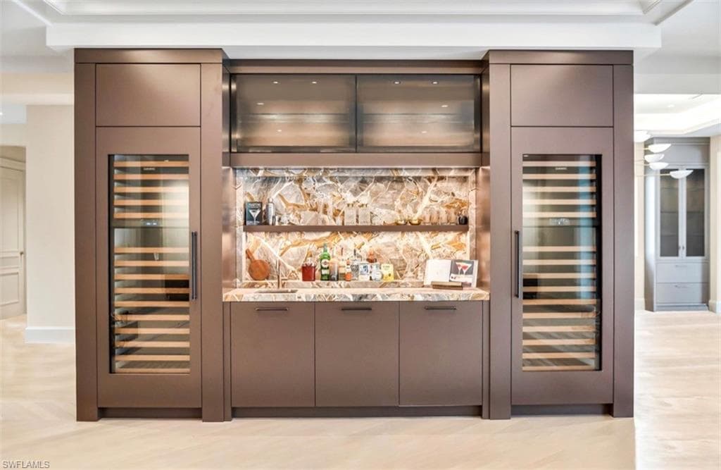 Built-in wet bar featuring stone backsplash, 2 integrated Subzero wine refrigerators, under-cabinet lighting, and custom cabinetry with hardware