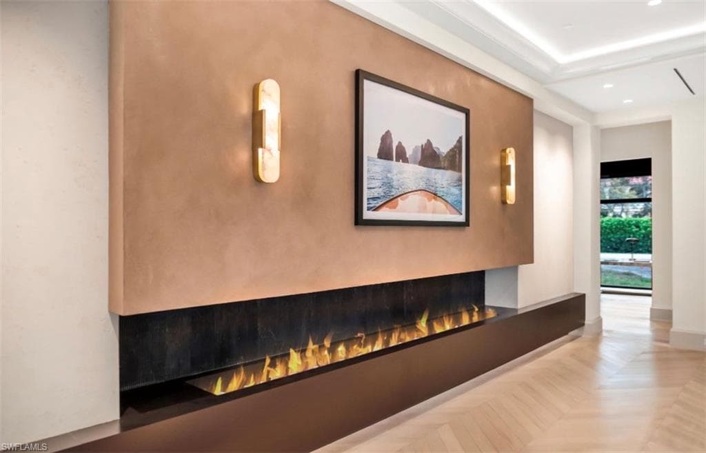 Linear gas fireplace, chevron wood flooring, Venetian plaster accent wall, and lit tray ceiling