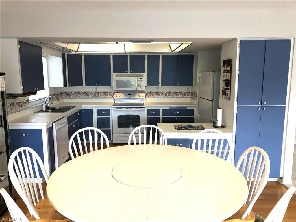 Kitchen with white appliances, blue cabinets, light countertops, and wood finished floors
