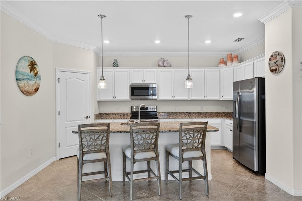 Kitchen featuring ornamental molding, a center island with sink, white cabinetry, dark stone countertops, and stainless steel appliances