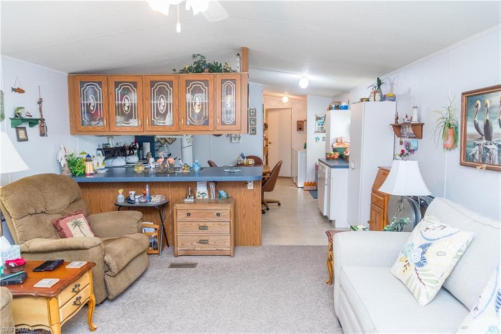 Living area with light colored carpet, lofted ceiling, and ceiling fan