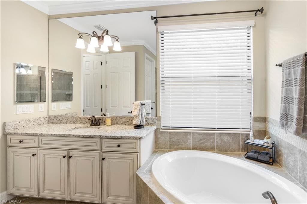 Full bathroom with vanity, ornamental molding, a garden tub, and a chandelier