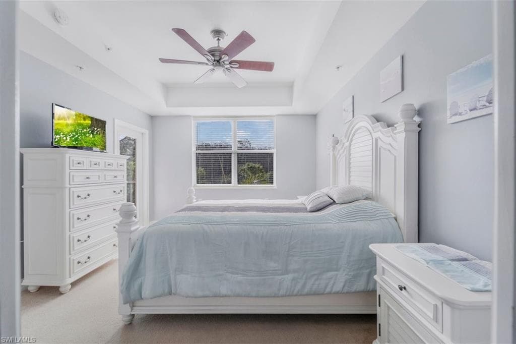 Bedroom featuring light carpet, a raised ceiling, and ceiling fan