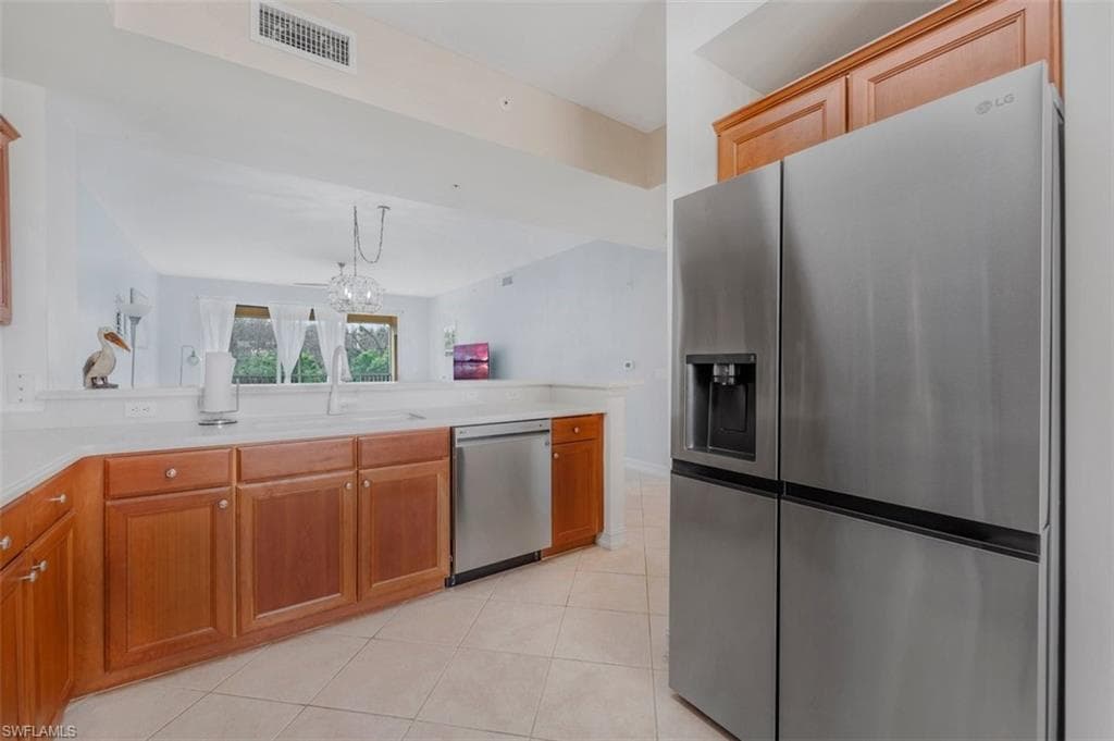 Kitchen featuring stainless steel appliances, wood finish cabinetry, light tile patterned flooring, a peninsula, and light stone countertops