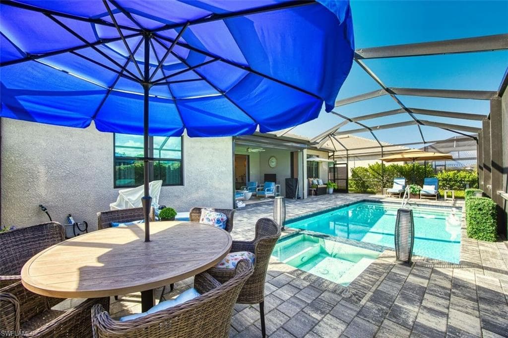 Combined pool / hot tub with a sunroom, a patio area, glass enclosure, and outdoor dining area