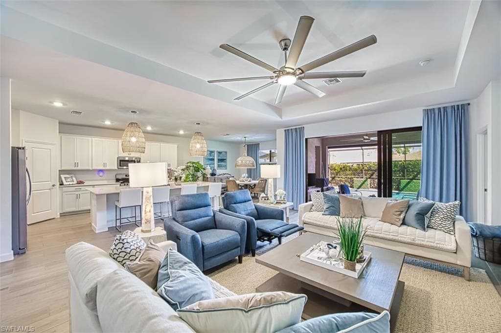 Living area featuring a ceiling fan, a tray ceiling, light wood-style floors, and recessed lighting