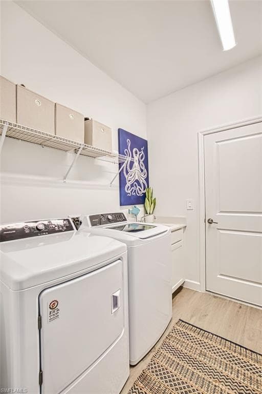 Laundry room with washing machine and clothes dryer, light wood-type flooring, and cabinet space