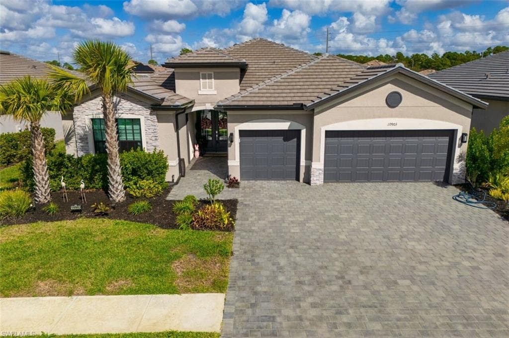 View of front of home featuring an attached garage, stucco siding, decorative driveway, and stone siding