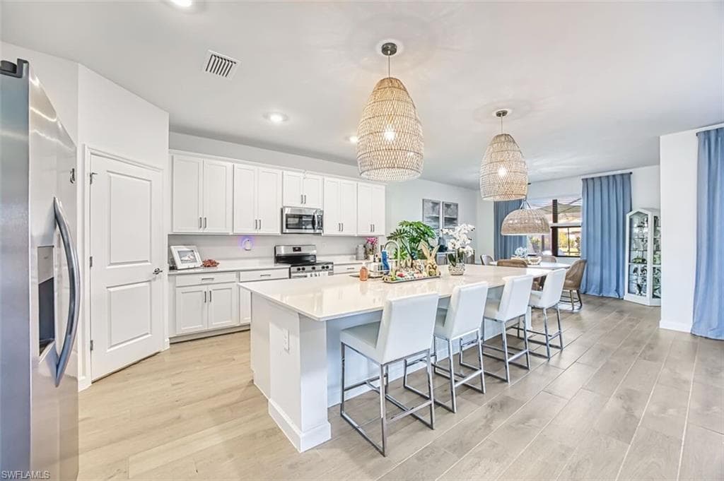 Kitchen with light wood finished floors, stainless steel appliances, white cabinetry, a large island with sink, and a breakfast bar