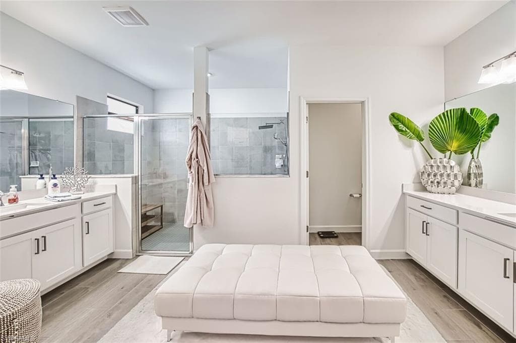 Bathroom featuring wood finish floors, two vanities, and a shower stall