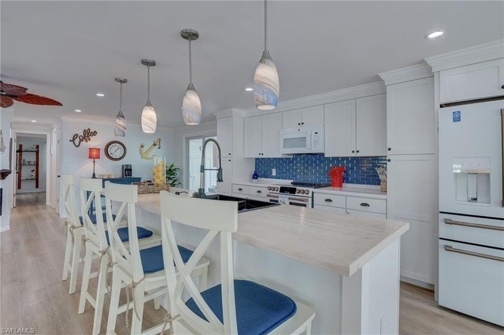 Kitchen with a breakfast bar, white appliances, white cabinetry, light wood-style flooring, and an island with sink