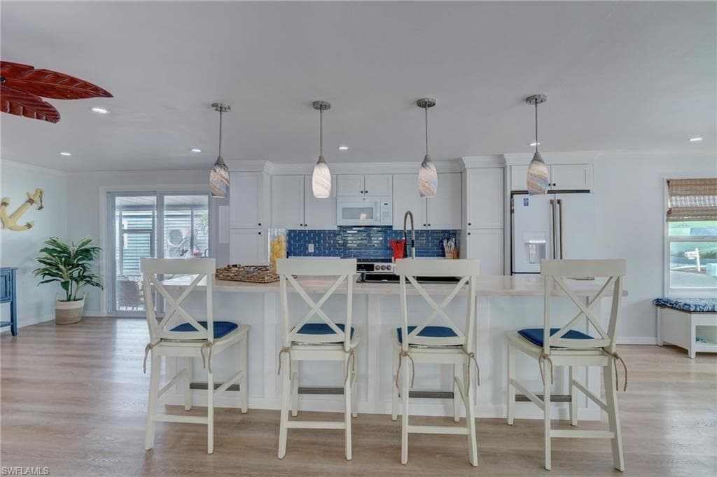 Kitchen featuring white cabinetry, white appliances, a breakfast bar, ornamental molding, and tasteful backsplash