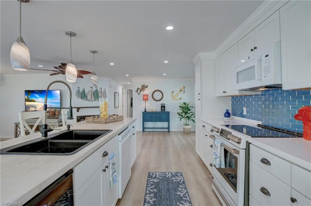 Kitchen with white appliances, white cabinetry, light wood-style flooring, ceiling fan, and pendant lighting