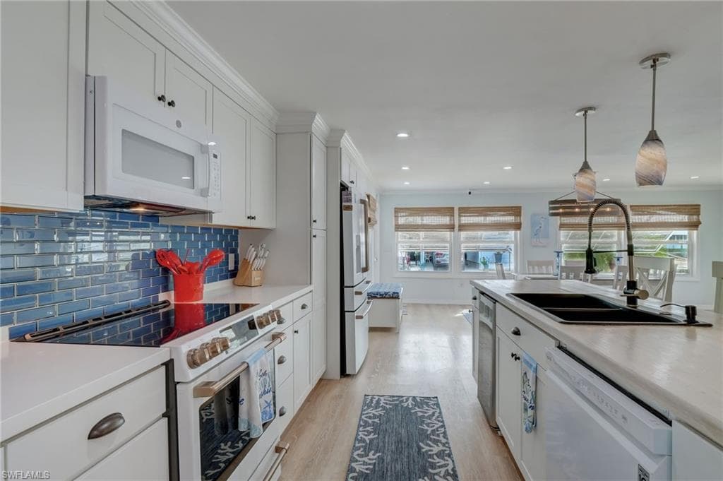 Kitchen with white appliances, white cabinetry, light countertops, light wood finished floors, and ornamental molding